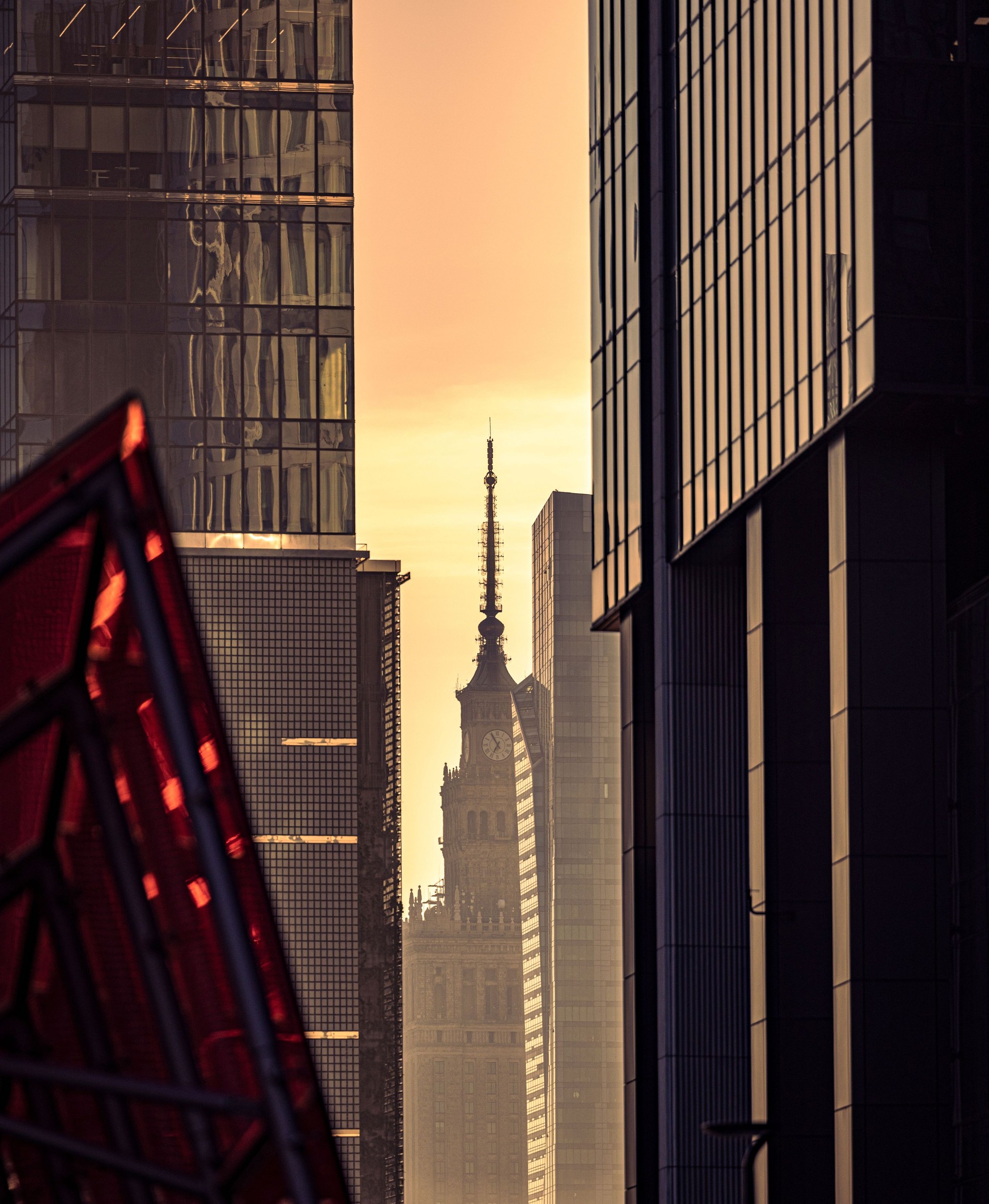 Old clock tower visible through new modern glass skyscrapers at the golden sunset in Warsaw,Poland